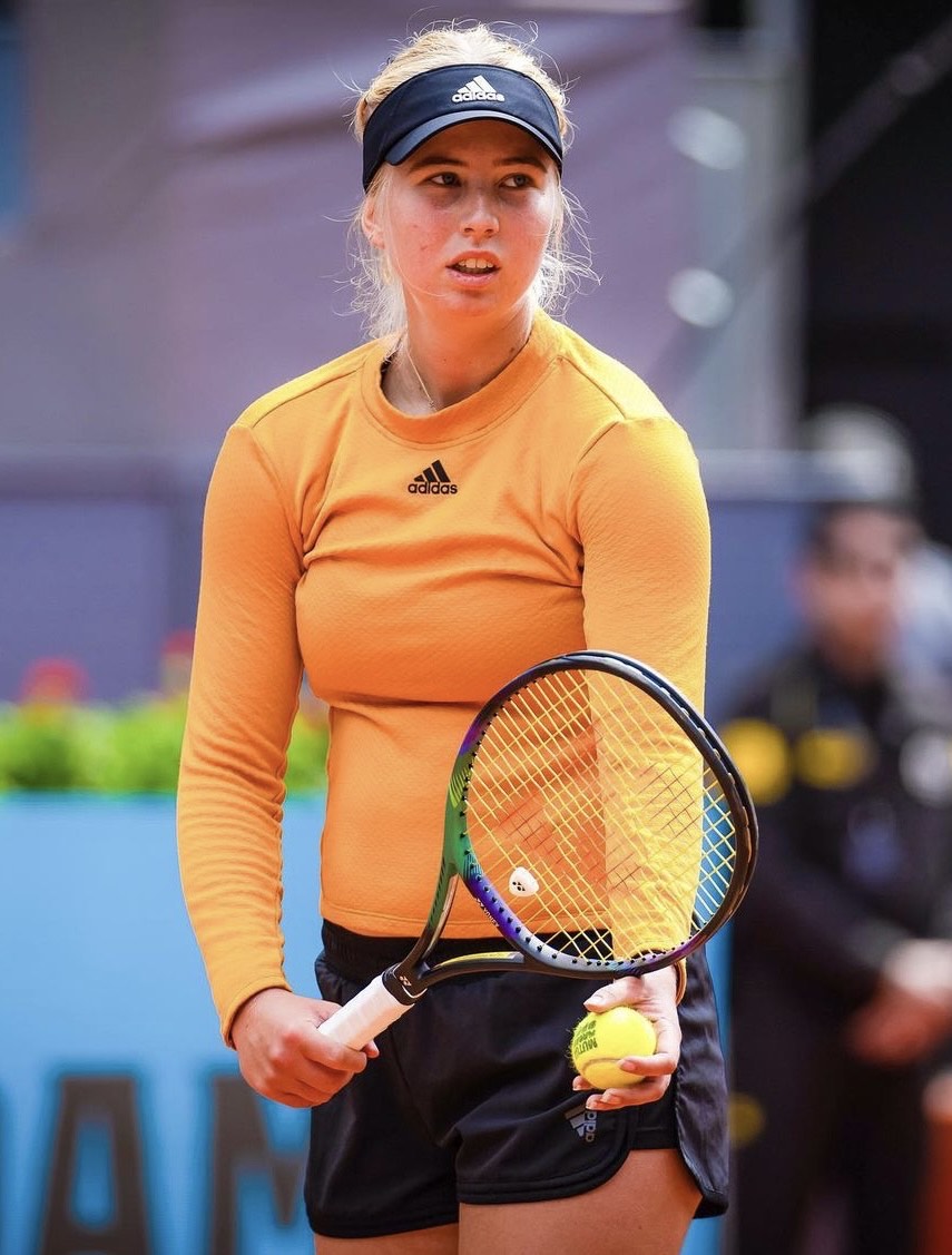 Tennis player in an orange shirt on a clay court, holding a racket.